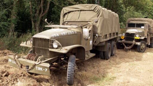 Zwei olivgrüne Militärlastwagen der US-Armee aus dem Zweiten Weltkrieg, geparkt in einem Waldgebiet.